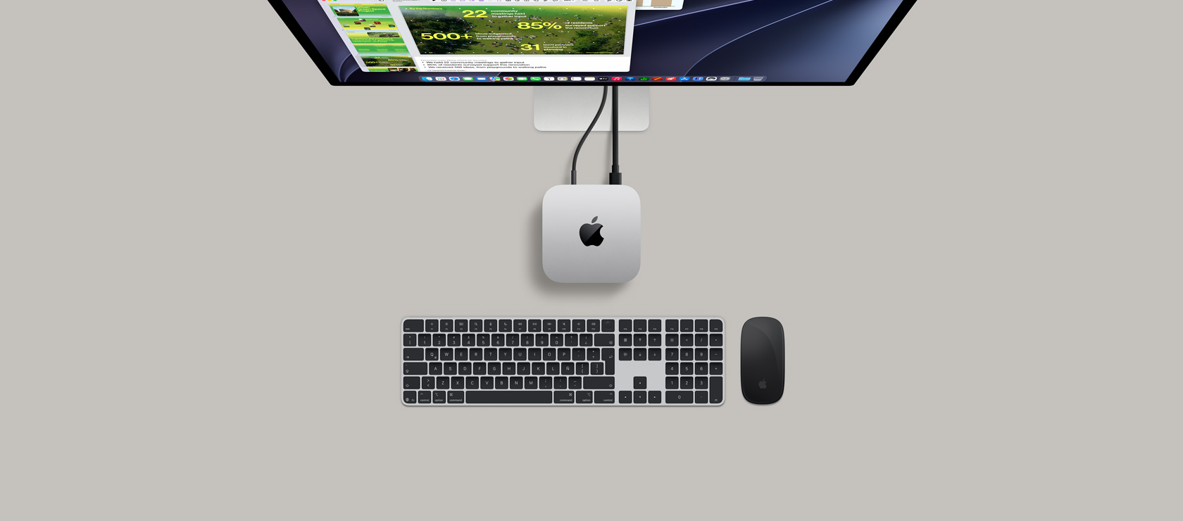 Mac mini, parte superior, aluminio color plata, esquinas redondeadas, logo de Apple en el centro en color negro brillante, conectada con un cable, monitor Studio Display parcialmente visible en la parte superior con la app Calendario, una presentación de Keynote y una gráfica de barras, Magic Keyboard con teclado numérico, Magic Mouse debajo de la Mac mini