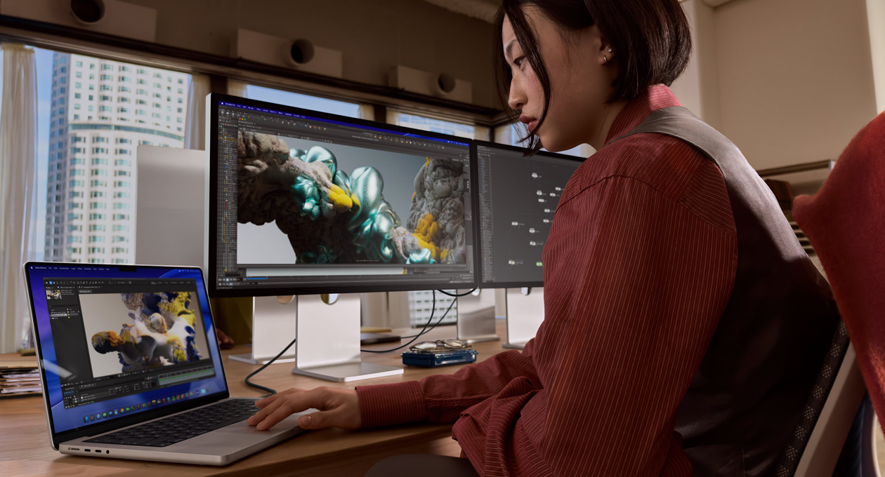 Une personne dans un bureau travaillant sur un MacBook connecté à un Studio Display XDR via un port Thunderbolt 5
