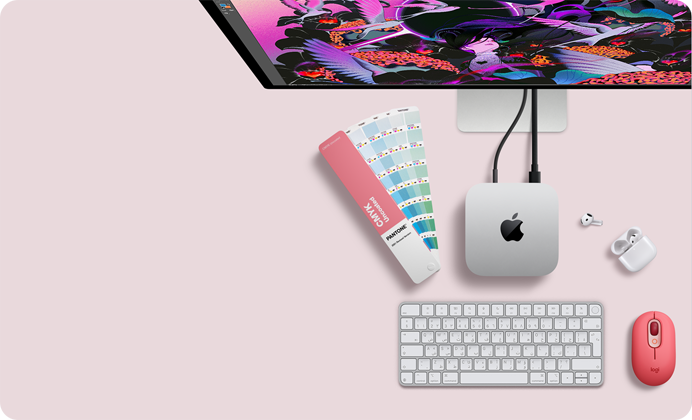 جهاز Mac mini، الجهة العلوية، ألومنيوم فضي، زوايا مدورة، شعار Apple باللون الأسود اللامع في الوسط، متصل بسلك، شاشة Studio Display تظهر بشكل جزئي في الأعلى، سماعات AirPods 4، مفتوحة، عينات ألوان Pantone، ولوحة مفاتيح رقمية وماوس