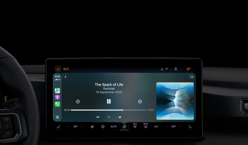 A car interior, centre console display shows Apple Podcasts playing via CarPlay, now playing ‘The Spark of Life’ podcast by Radiolab, playback controls include skip back, pause and skip forward.