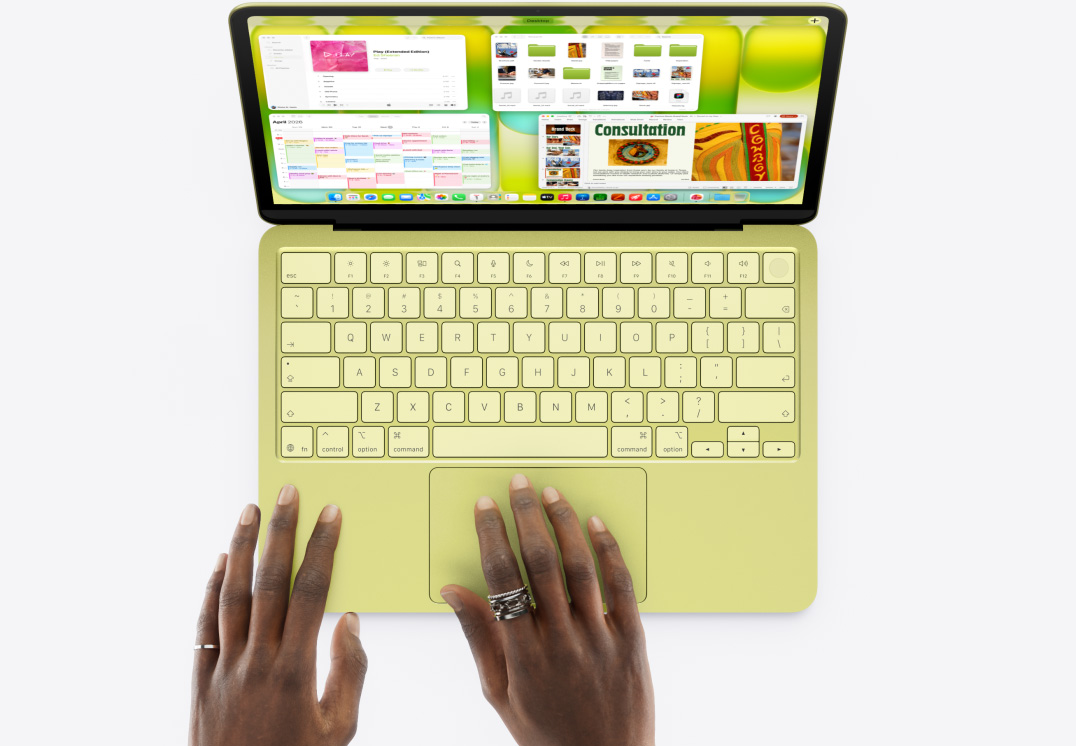 MacBook Neo w kolorze cytrusowożółtym, dłoń dotyka gładzika, otwartych jest wiele okien, w tym aplikacje Muzyka, Kalendarz i Microsoft PowerPoint