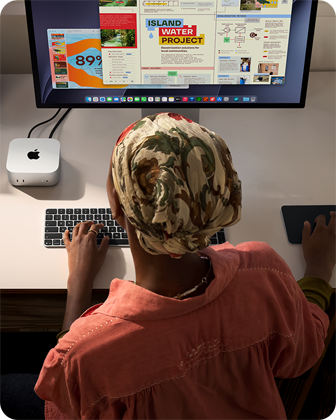 O persoană tastând la un birou cu un Mac mini, Studio Display conectat, Magic Keyboard, Magic Trackpad, diverse obiecte