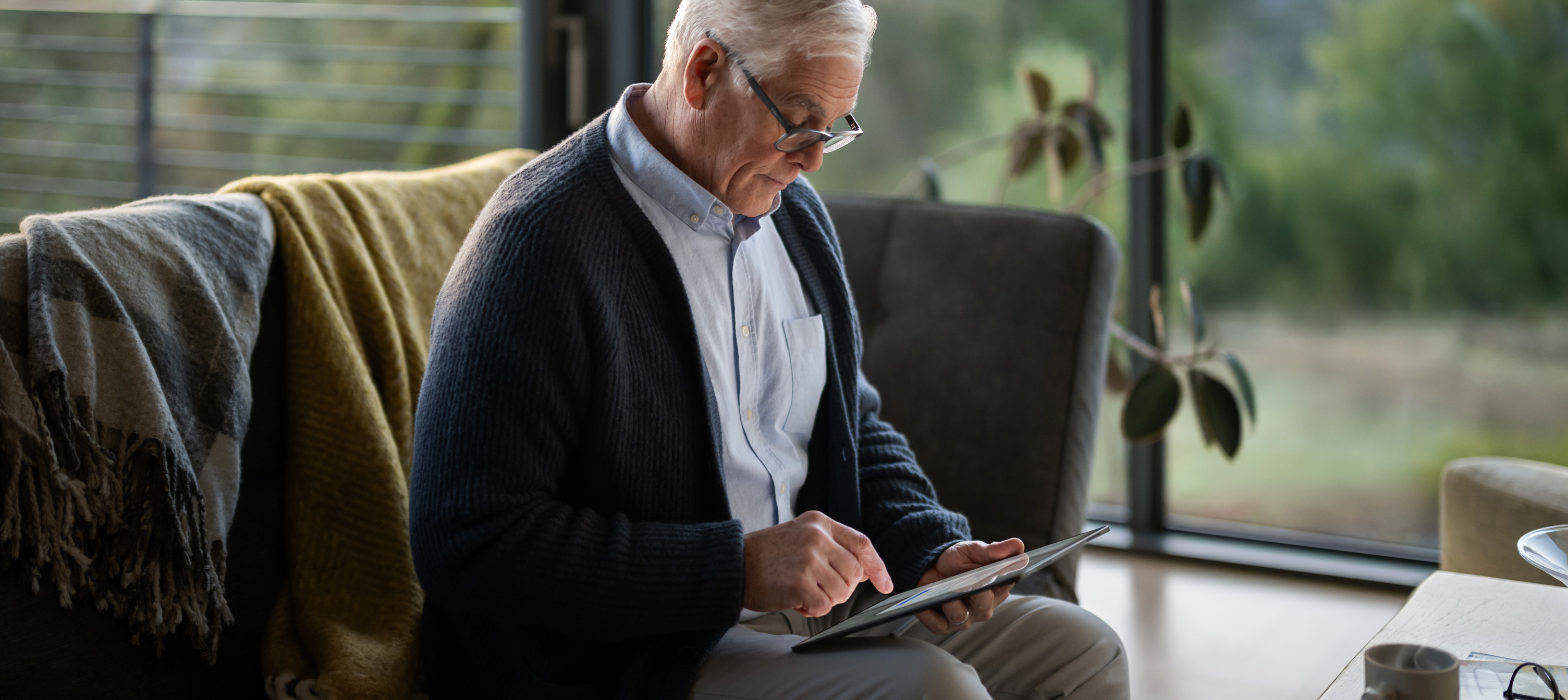 رجل مسن يجلس على أريكة ينظر إلى جهاز iPad.‏