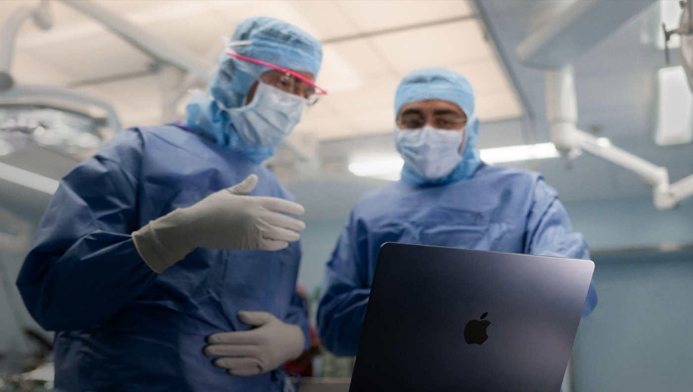 Two surgeons discussing something on the screen of a MacBook Pro in the operating theatre.