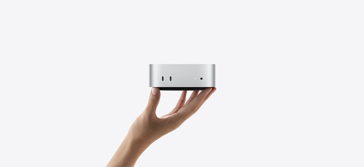 Изглед отпред на Mac mini, балансиран на върха на пръстите на изпъната ръка, отпред са два Thunderbolt порта, светлинен индикатор и жак за слушалки, конусовидна черна основа отдолу, плосък отгоре, заоблени страни, прави ръбове, цвят сребърно