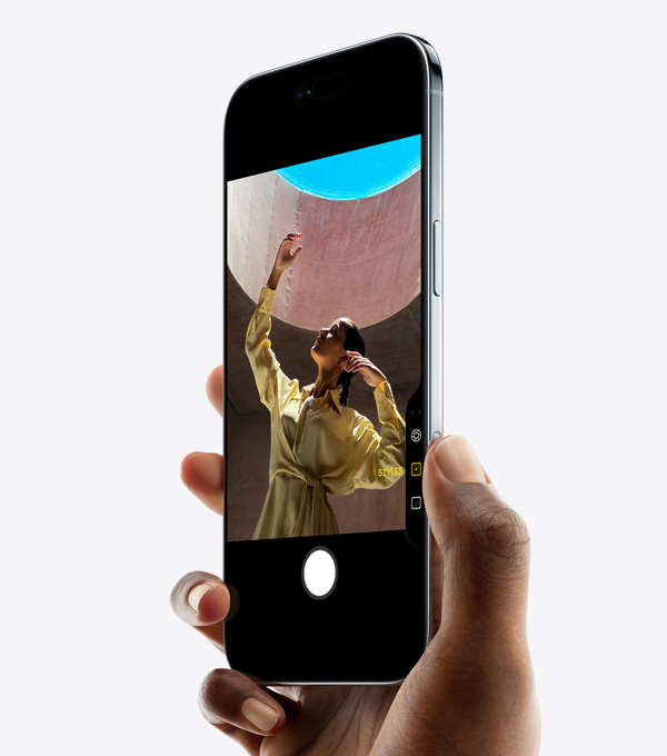 Ruka držící iPhone Air, palec je na ovladači fotoaparátu, šikmý pohled zepředu, tenký profil, Dynamic Island, boční tlačítko