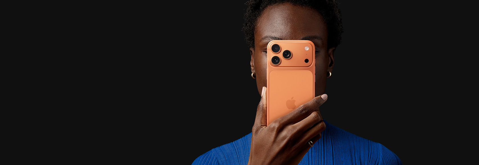 A person holds iPhone 17 Pro in front of their face, back exterior facing outward, Cosmic Orange colour