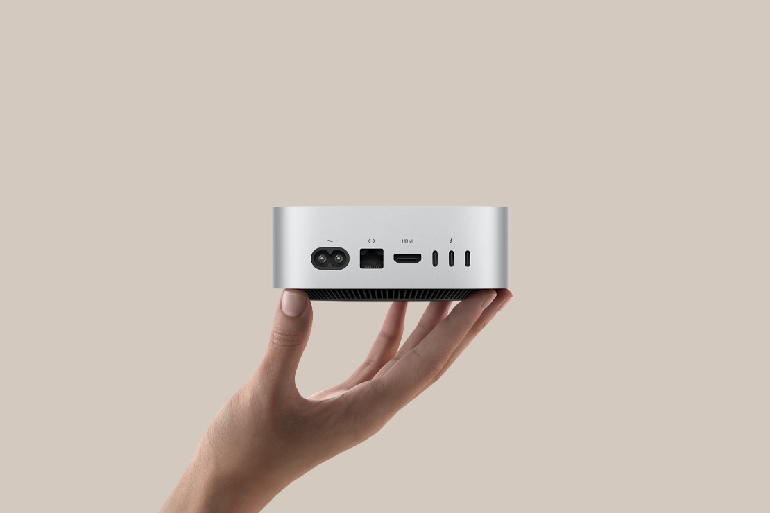 Hõbedane Mac mini, mille tagumised liidesed on nähtaval ja mis toetub sõrmeotstele