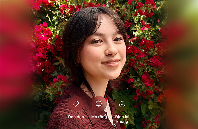 Ảnh chụp một người có mái tóc nâu, đang mỉm cười, mặc áo len nâu, xung quanh là hoa đỏ, minh họa chỉnh sửa ảnh bằng AI với các tùy chọn Dọn Dẹp, Mở Rộng, Định Lại Khung hiển thị trên ảnh